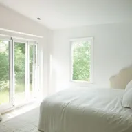 Bright and airy bedroom with white walls, light colored bedding, and large windows letting in natural sunlight