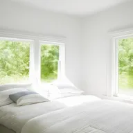 Bright and airy bedroom with white walls, light colored bedding, and large windows letting in natural sunlight