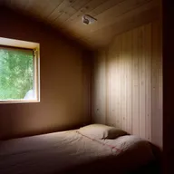 A cozy bedroom with low-height walls and a single, small window minutely illuminating the room.