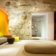 A spacious 4m by 8m room featuring a massive natural rock wall with heavy relief, subtly lit by indirect light and a mirror seamlessly incorporated. Dominating the room is a large, minimalist white sofa adorned with yellow pillows, complemented by a Karim Rashid coffee table.