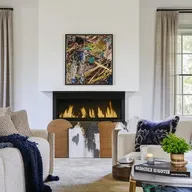 A well-decorated living room featuring a plush couch, a coffee table with magazines, a fireplace, and walls adorned with stunning wall art.