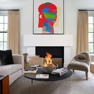 A well-decorated living room featuring a plush couch, a coffee table with magazines, a fireplace, and walls adorned with stunning wall art.