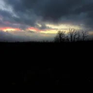 A moody landscape at dawn, depicting ashes scattered across a darkened scene as the first light of day struggles to break through the heavy overcast sky