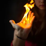A close-up image focusing on the hand and wrist of a young girl, around the age of 16, with fire blazing brightly in her palm